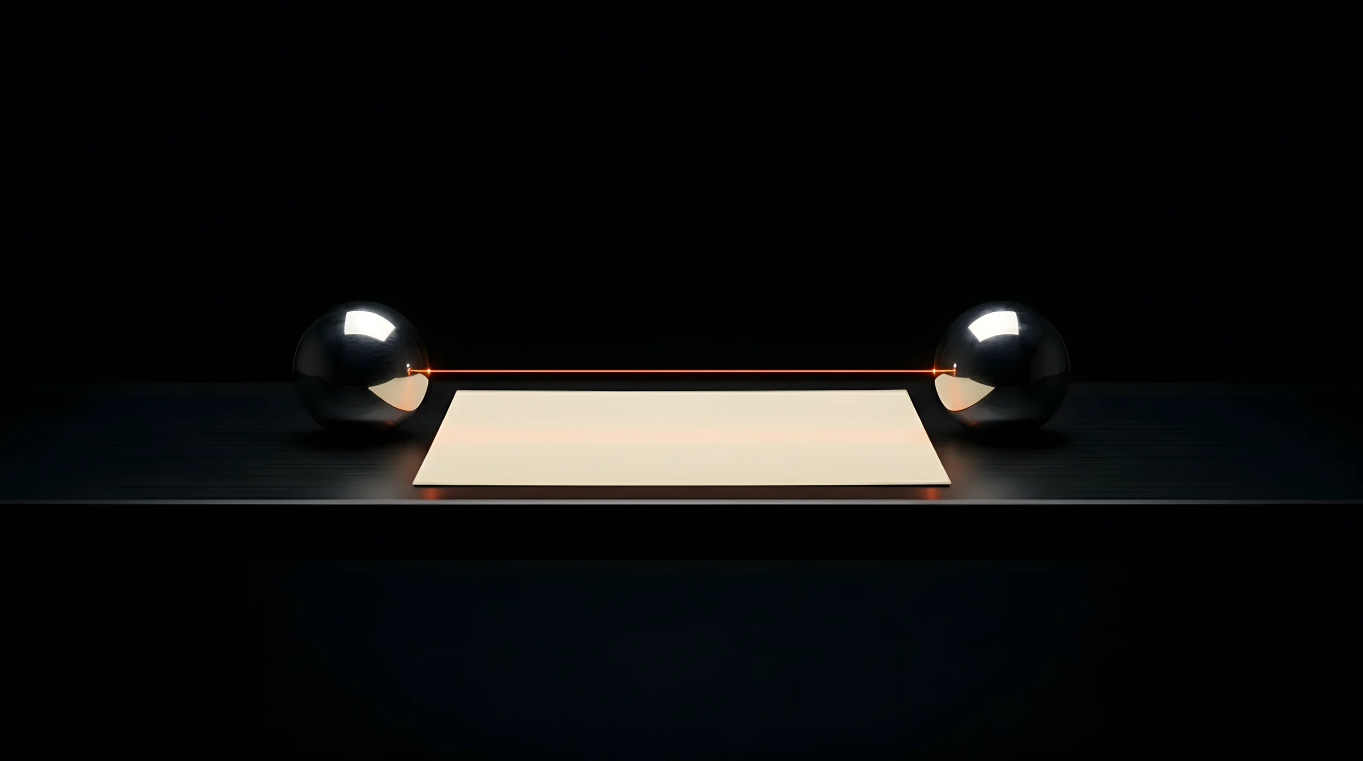Two polished steel spheres facing each other across a black table, joined by a thread of orange light over one sheet of paper.